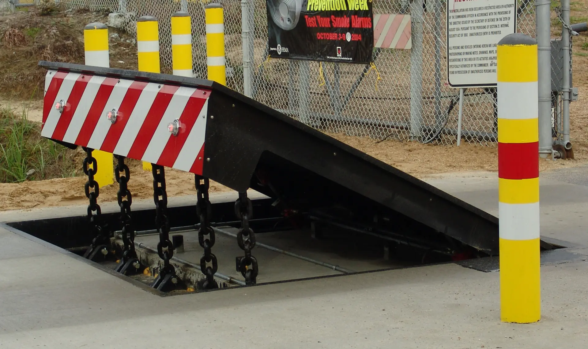 Raised security barrier with striped front and chain supports near yellow bollards.