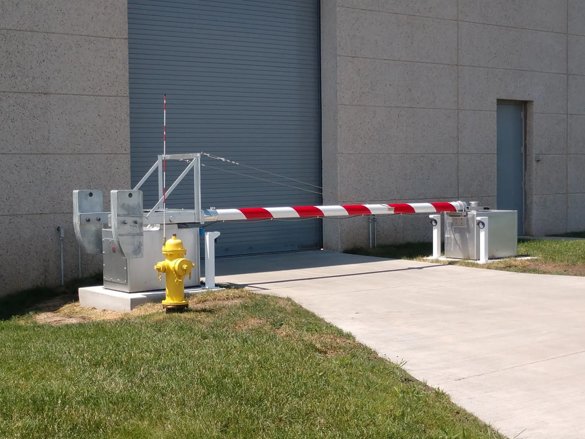 Automated barrier arm with red and white stripes blocks a concrete driveway by a yellow fire hydrant.