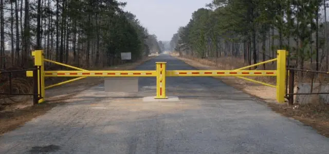 A yellow swing gate with red reflectors blocks access to a forest road.