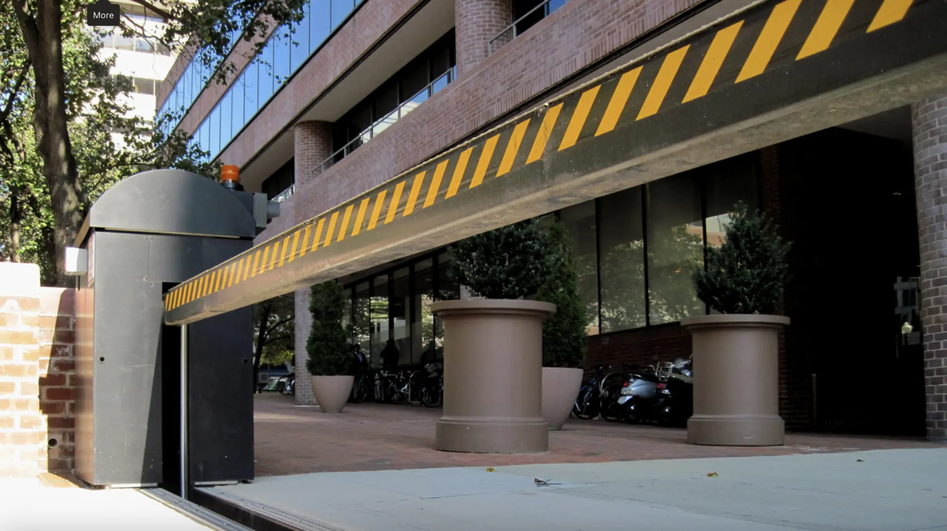 Security gate with yellow warning stripes extends near a brick building with reflective windows.
