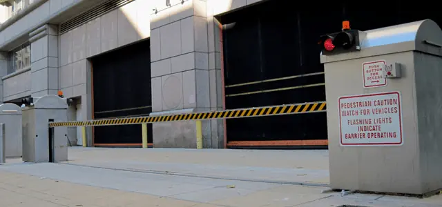 Yellow-and-black striped gate arm with flashing light and a warning sign at a secured entrance.