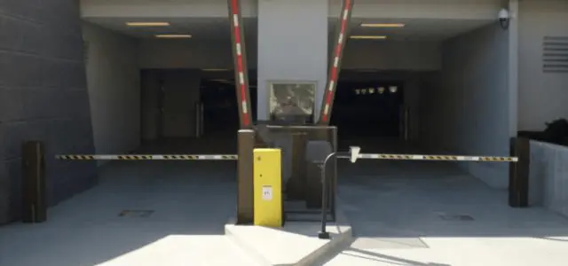 Dual gate arms with reflective stripes secure the entrance to a covered parking area with overhead lighting.