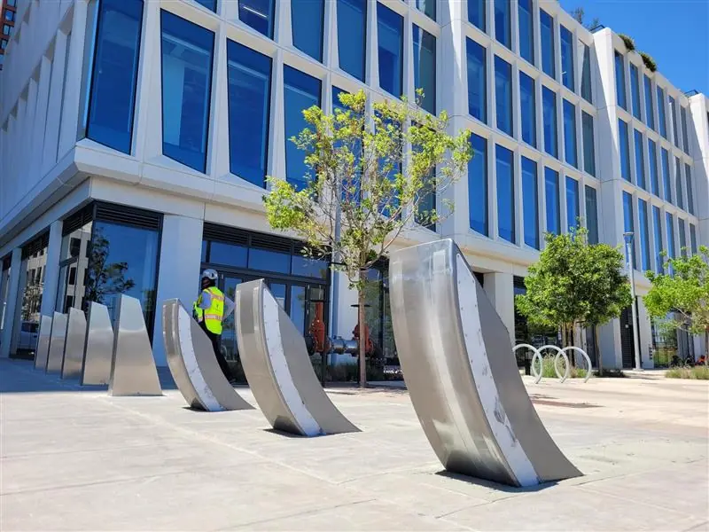 Silver metal bollards with a sleek design block access to a modern building entrance near trees.