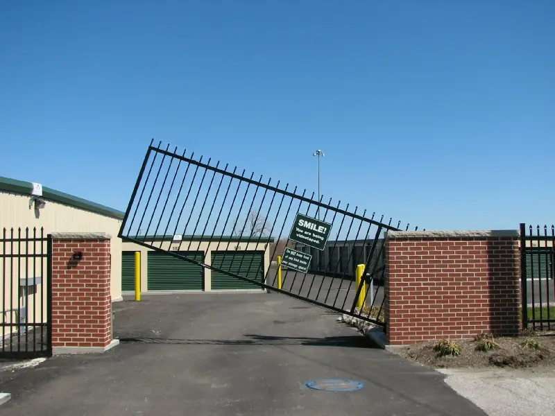 Tilted security gate with a "SMILE! You are being videotaped." sign beside storage units.