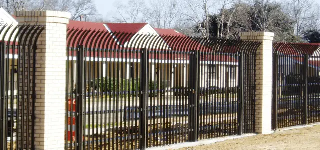 Black security fence with arched tops and brick columns encloses a residential area.