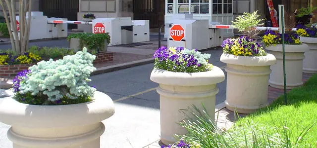 Flower-filled planters enhance the landscape around a checkpoint with stop signs and entry barriers.