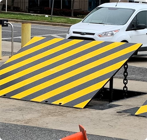 Wedge barrier with black and yellow stripes stands upright at a secured entry point.