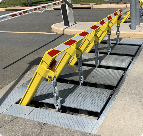 A yellow vehicle barrier with red reflective stripes and chains blocks entry to a secured area.
