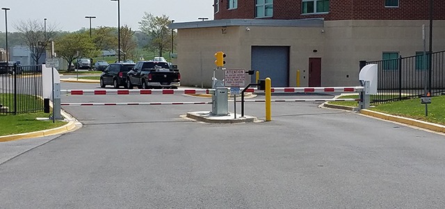 Automated barrier arm with red and white stripes secures access to a facility driveway.