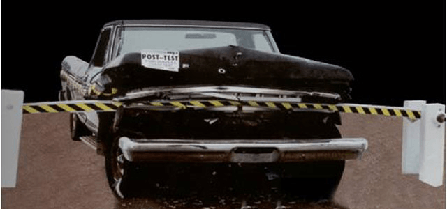 Vehicle impact test showing a truck crumpled against a sturdy striped barrier.