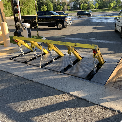 Raised yellow vehicle barrier with chains at an entry control point on a paved road.
