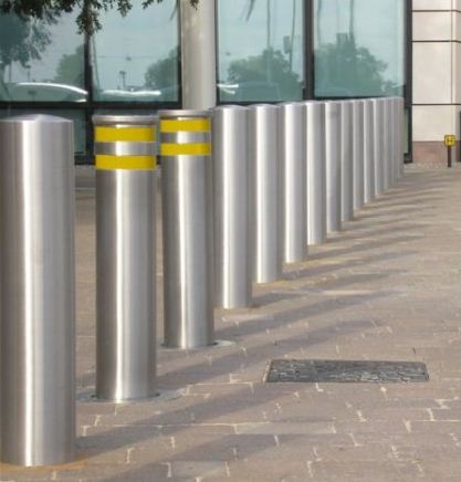 A line of silver metal bollards on a stone walkway, with two bollards marked by yellow bands.