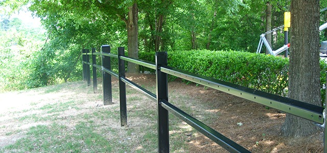 Black metal fencing with two horizontal rails encloses a landscaped, shady area.