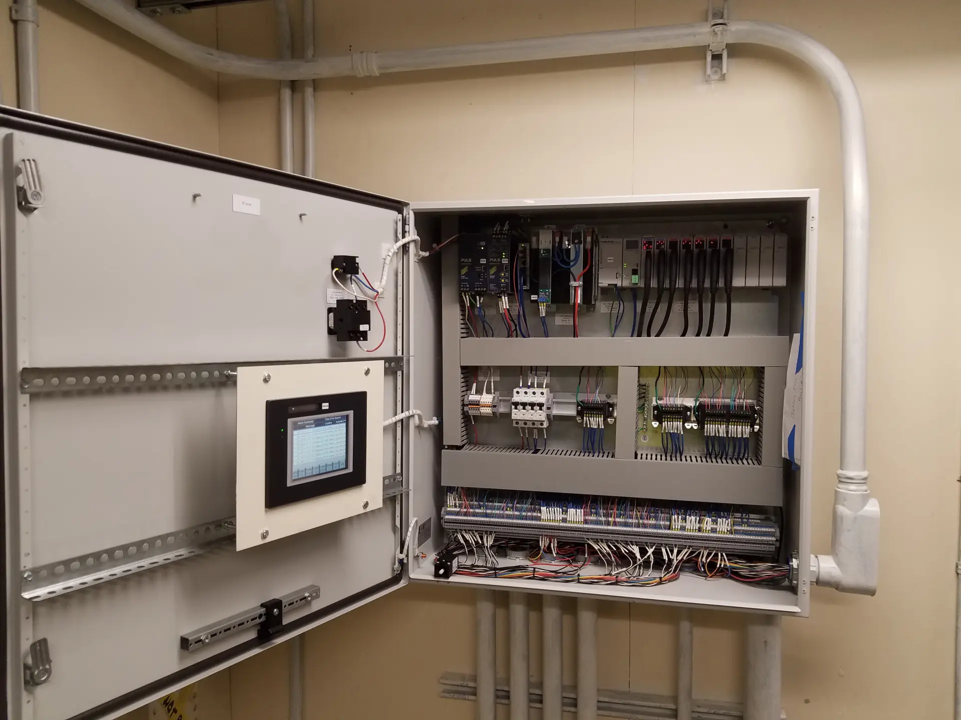 Open wiring panel in a utility room showing electrical connections and cables.