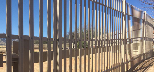 Beige metal fence with closely spaced vertical bars on a sunny day.