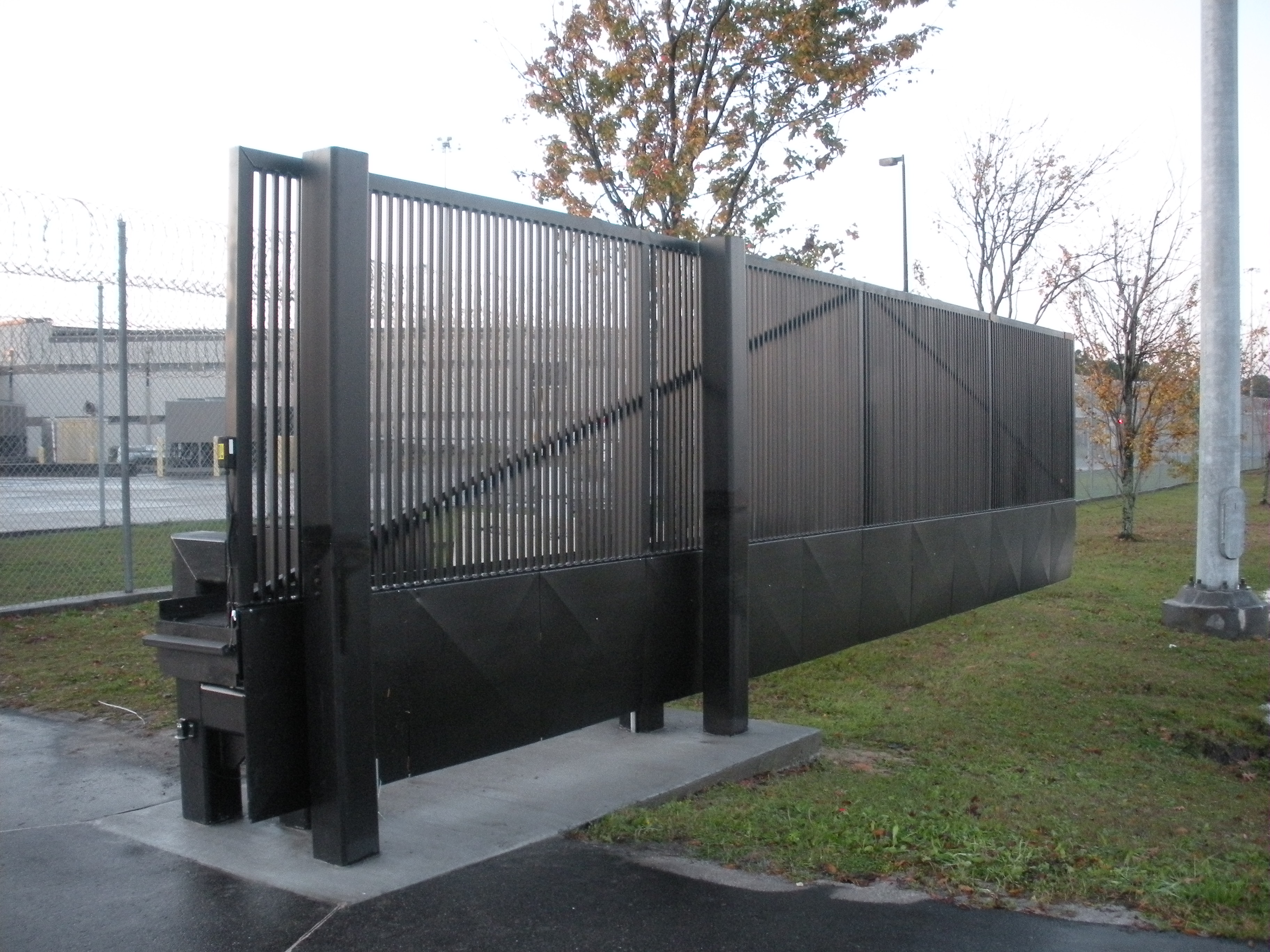 Black metal sliding gate at a secure facility entrance with vertical bars.