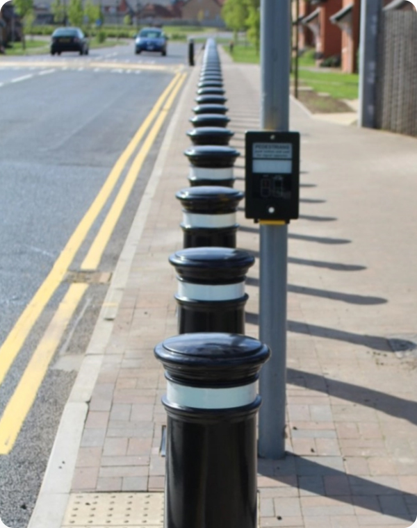Row of black and white bollards lining a paved sidewalk in an urban area.