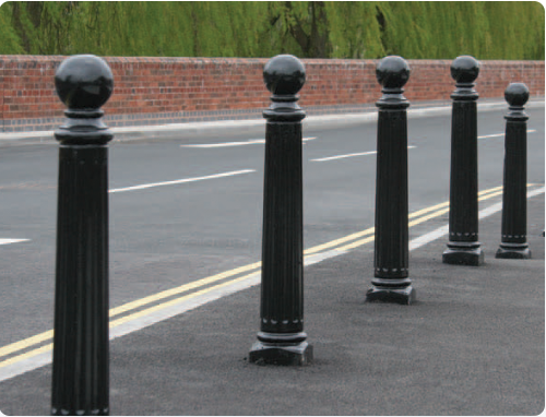 Decorative black bollards with rounded tops alongside a roadway.