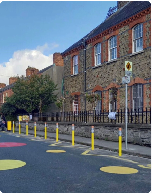 Row of yellow bollards near a brick building on a street with painted circles.