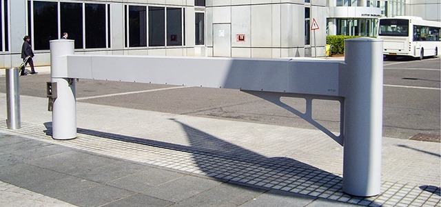 Modern white metal barrier arm across a paved entrance area.