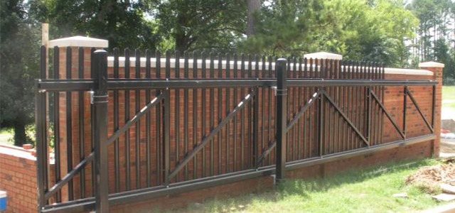 Black metal fence with vertical bars atop a brick wall in a landscaped area.