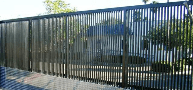 Tall black fence with narrow slats, creating a visually solid barrier around a building.