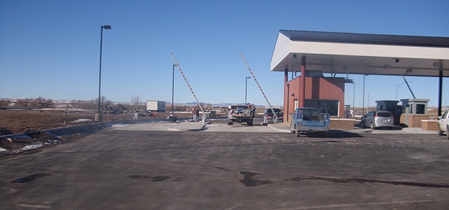 Checkpoint entrance with striped gate arms and a covered guard station in an open area.
