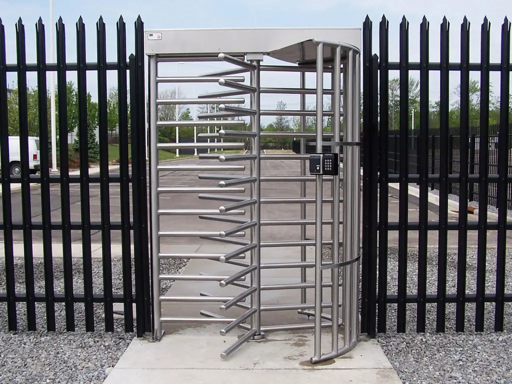 Full-height stainless steel turnstile gate installed between black vertical metal fencing.