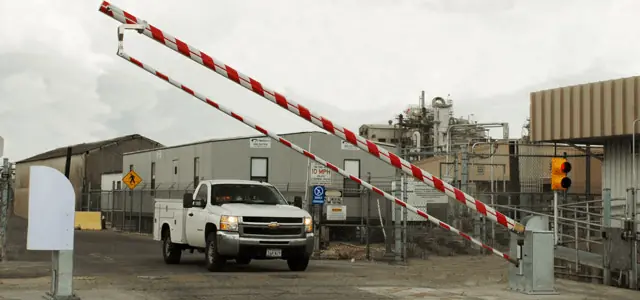 A red-and-white barrier arm raised at an industrial facility's entrance.
