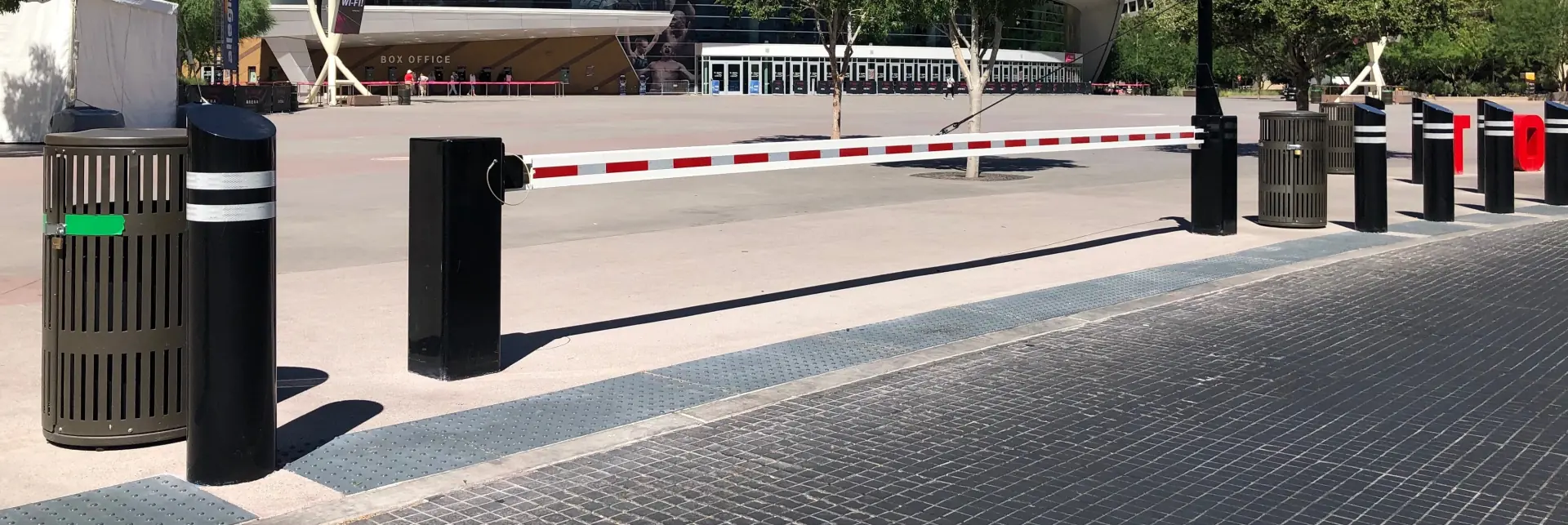 Lowered security gate arm with flashing light and pedestrian warning sign near a building entrance.