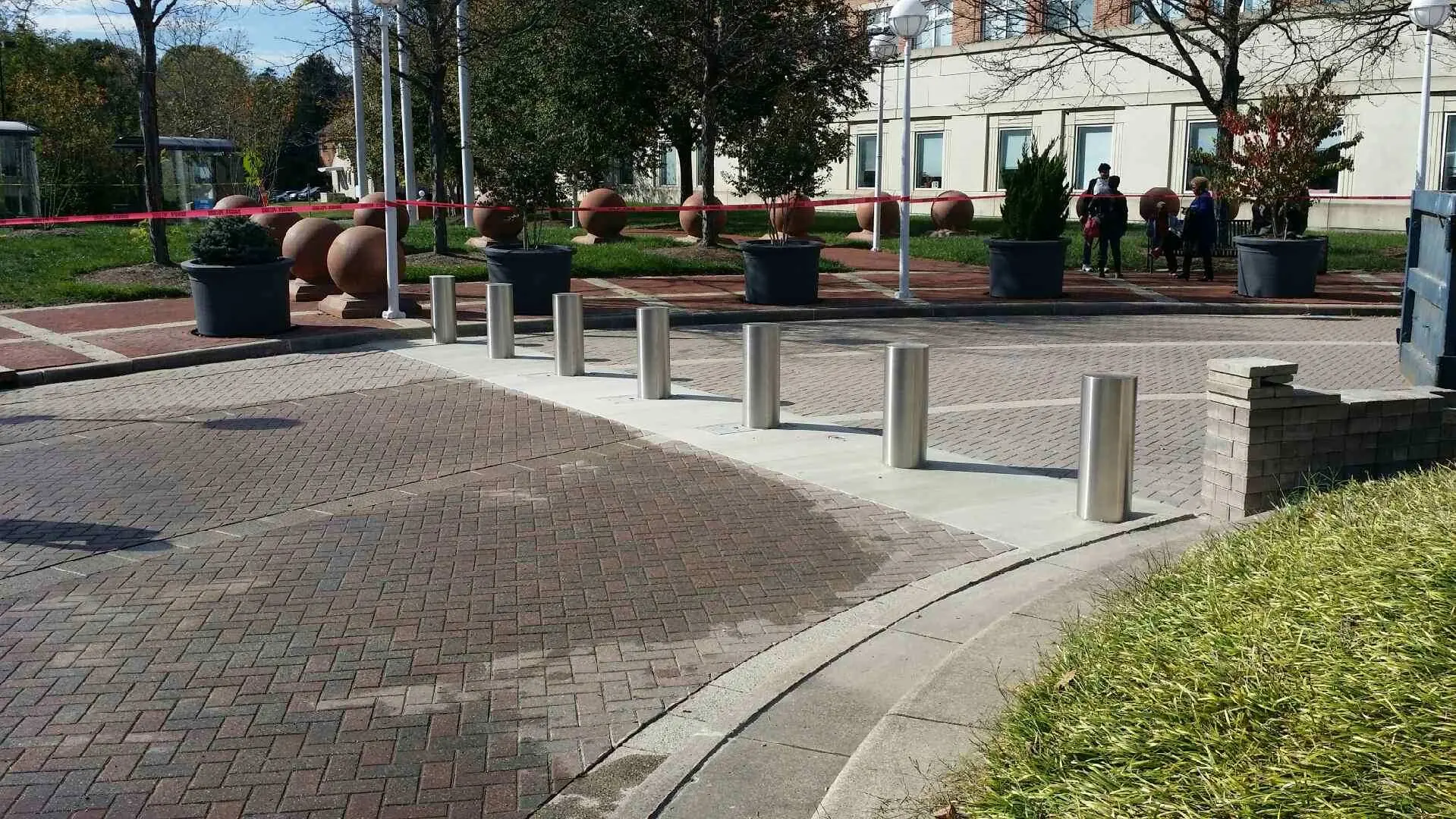 Row of stainless-steel bollards along a brick-paved area with planters and benches.