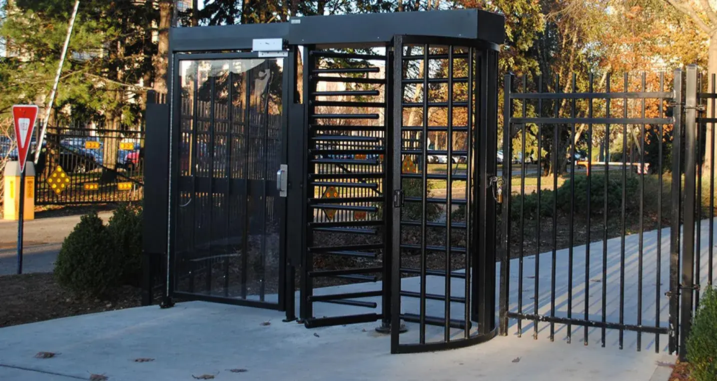 Black full-height turnstile gate with vertical bars installed at a secure facility entrance.