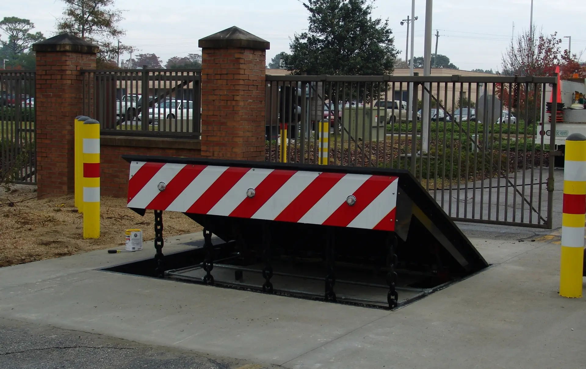 Red and white striped wedge barrier raised from the ground at a gated facility entrance.