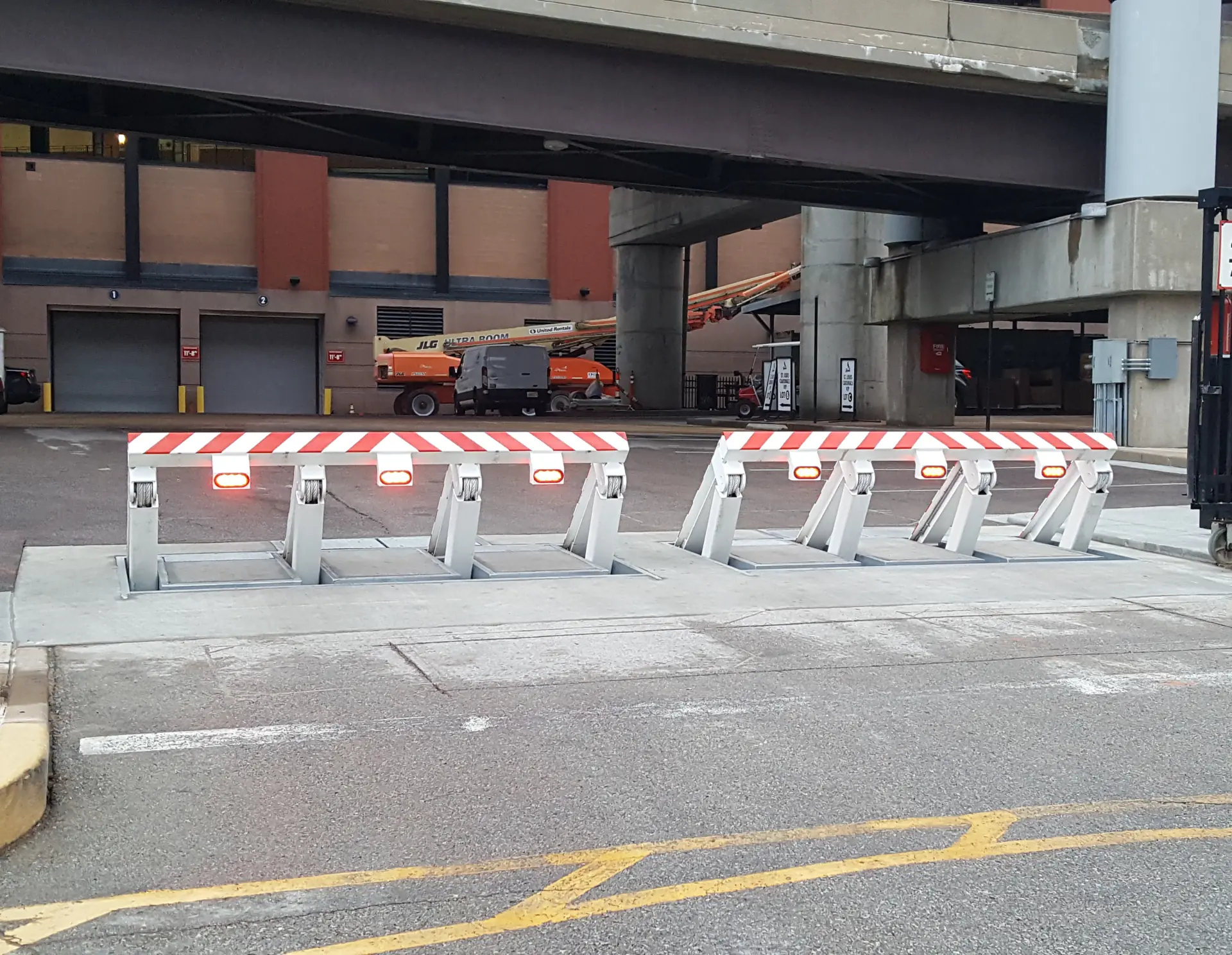 Multiple anti-ram wedge barriers with red lights and striped panels block a secure vehicle entrance.