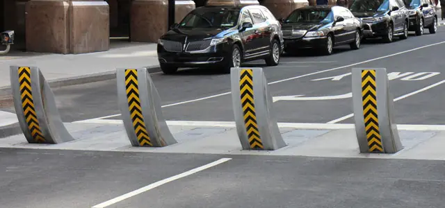 Four chevron-striped Raptor bollards in a road near parked cars.
