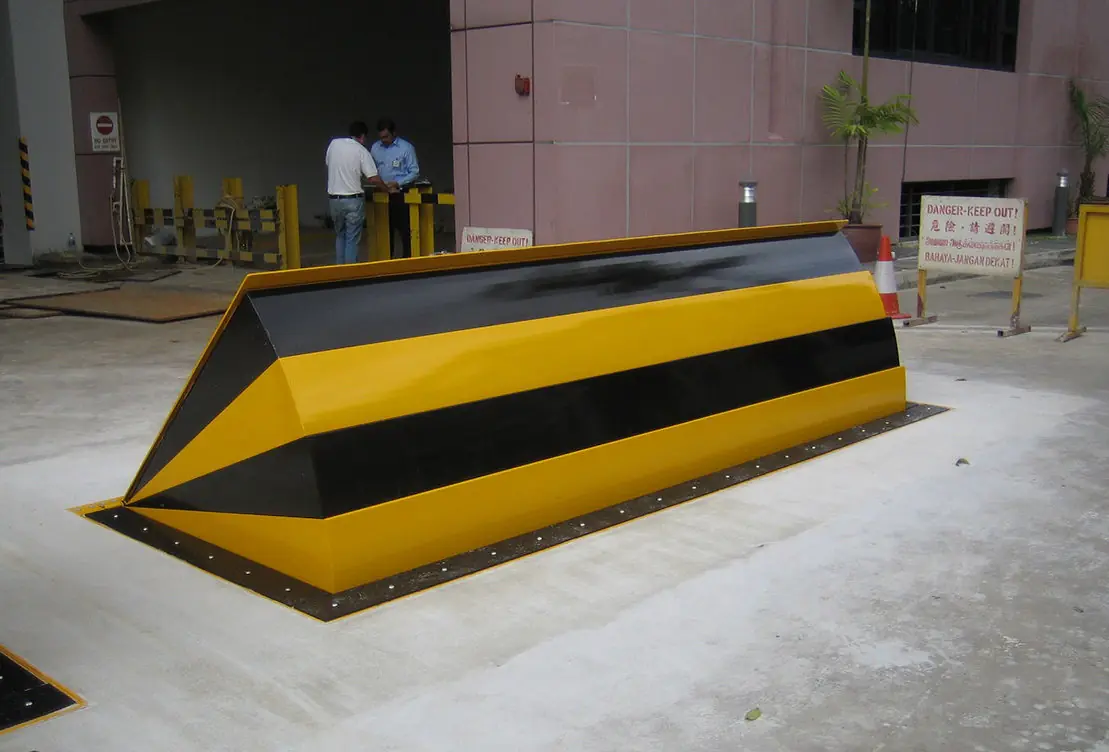 Triangular wedge barrier with yellow-and-black stripes for vehicle control at an entry point.