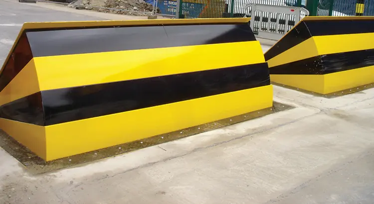 Heavy-duty wedge barriers with yellow and black stripes block an entryway.