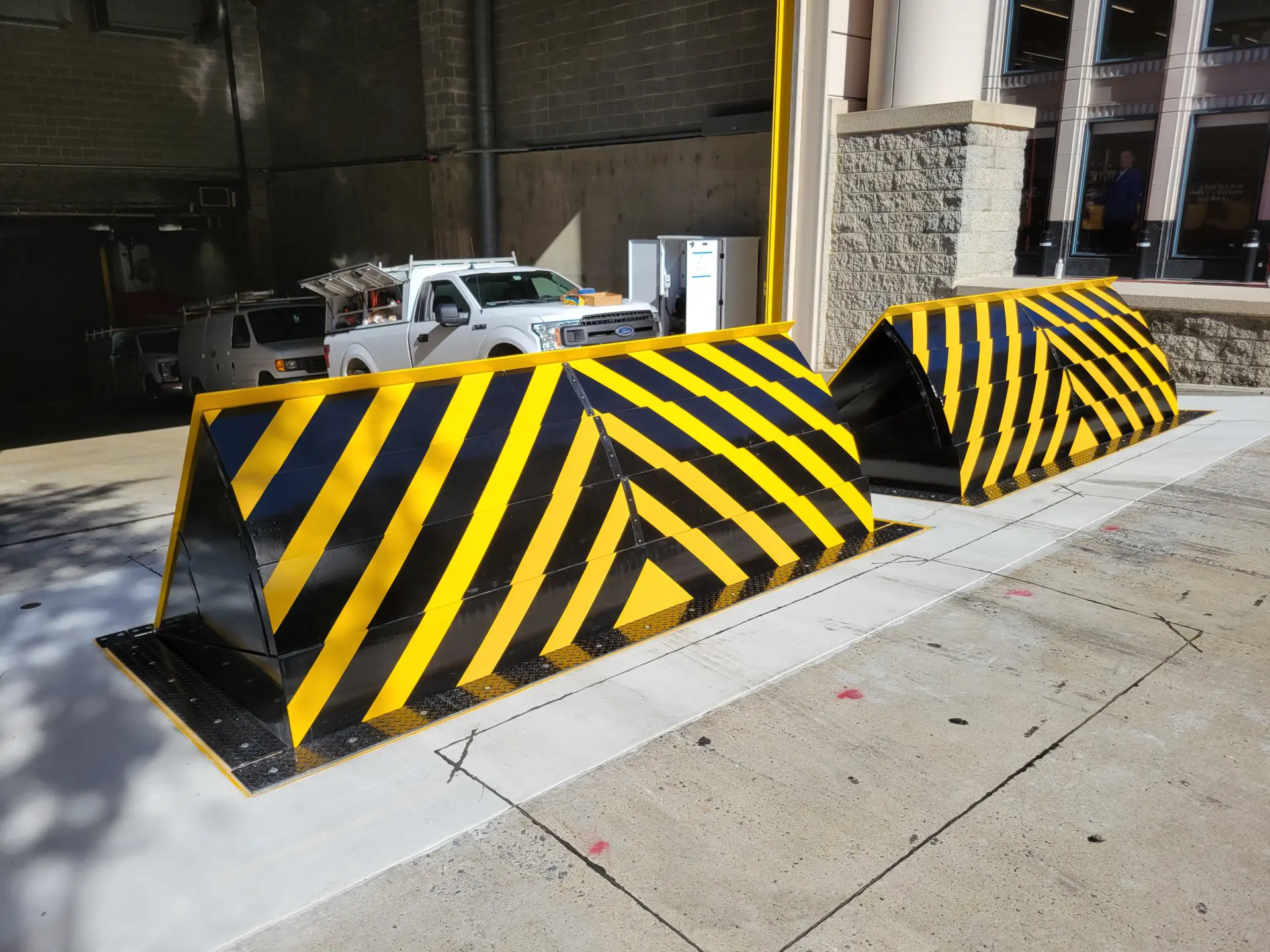 Heavy-duty vehicle barriers with diagonal hazard stripes outside a commercial loading area.