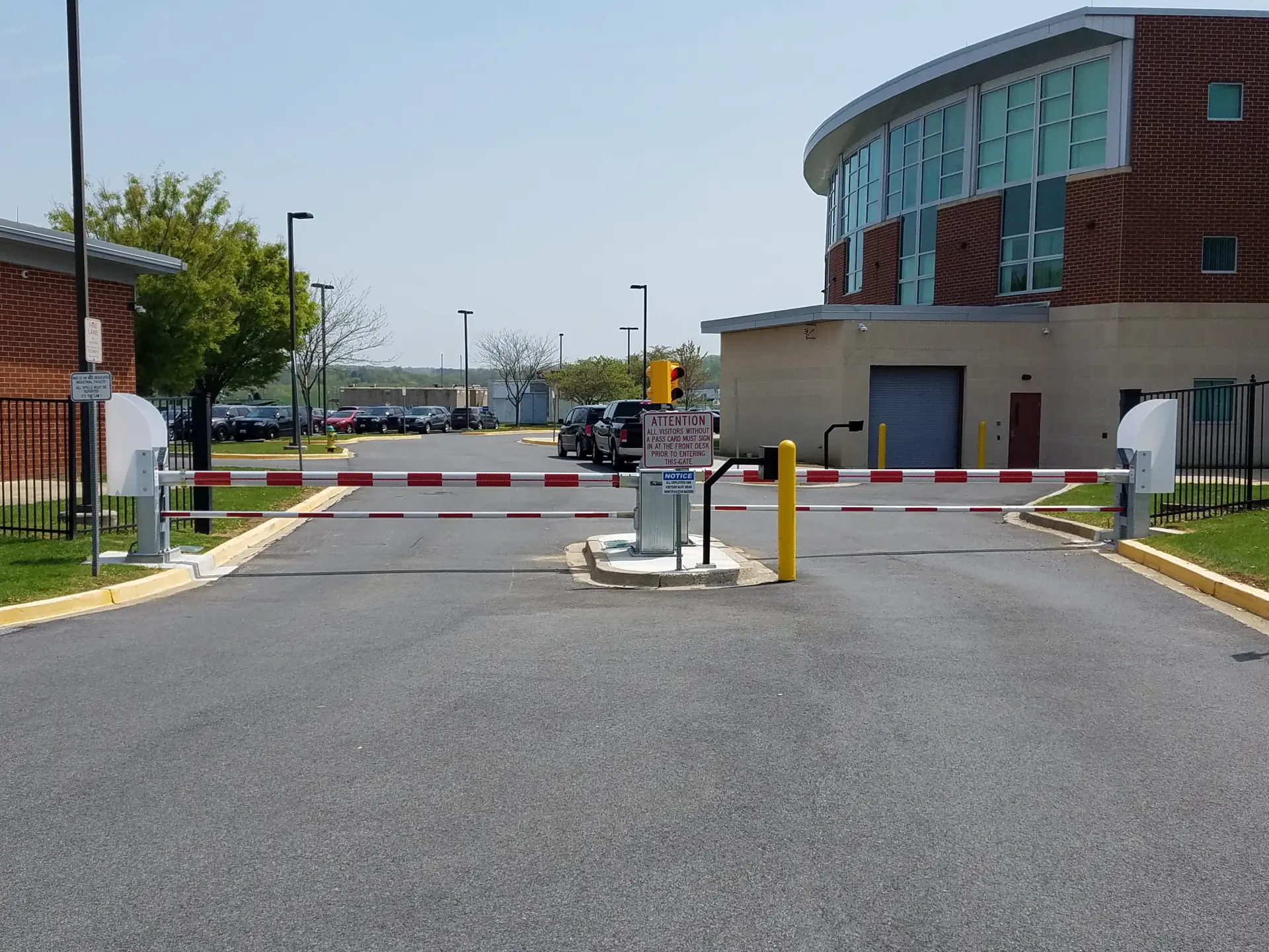 Red and white barrier arm blocks a two-lane driveway entrance between institutional buildings.