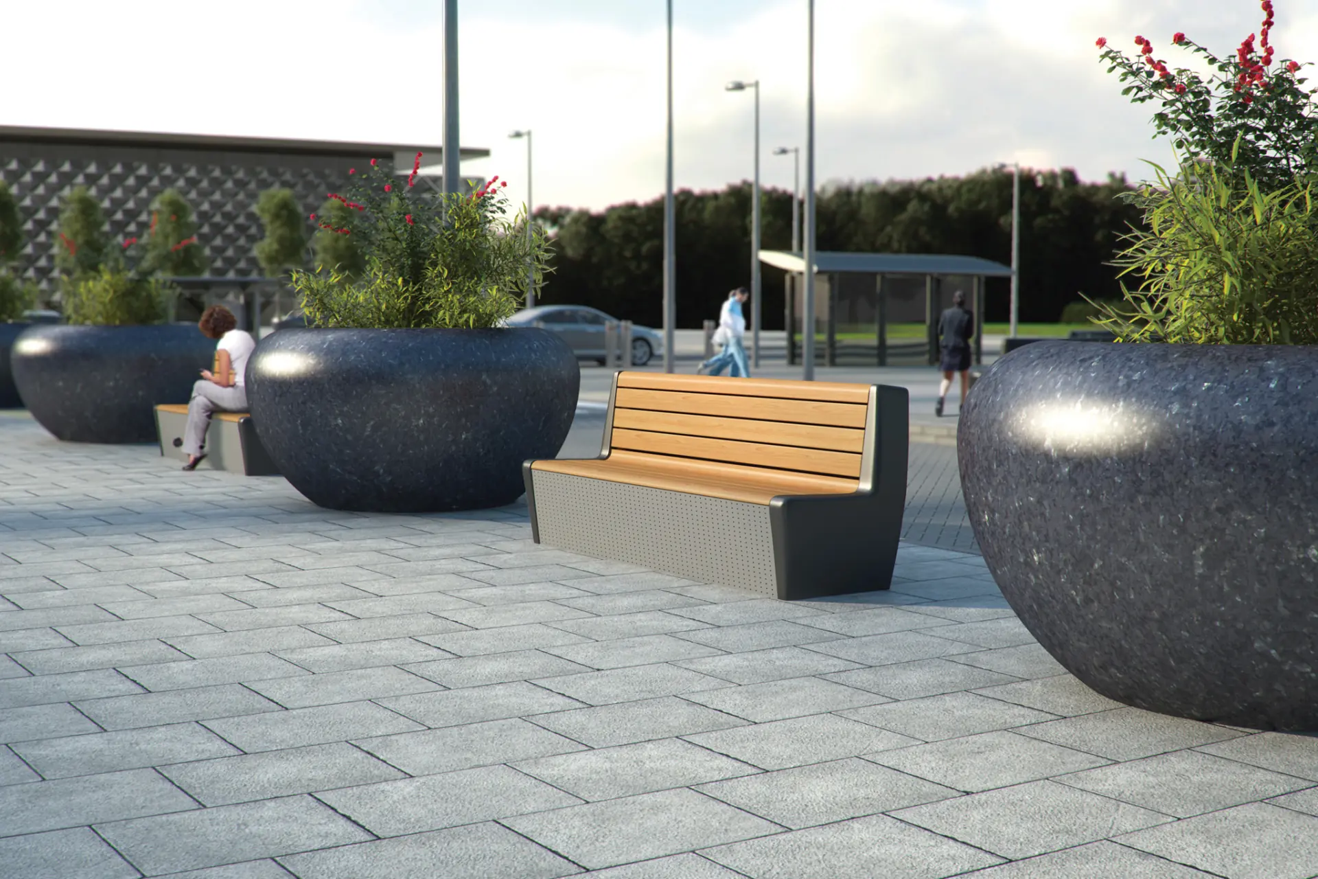 Wooden benches and large round planters with greenery line a paved public plaza.
