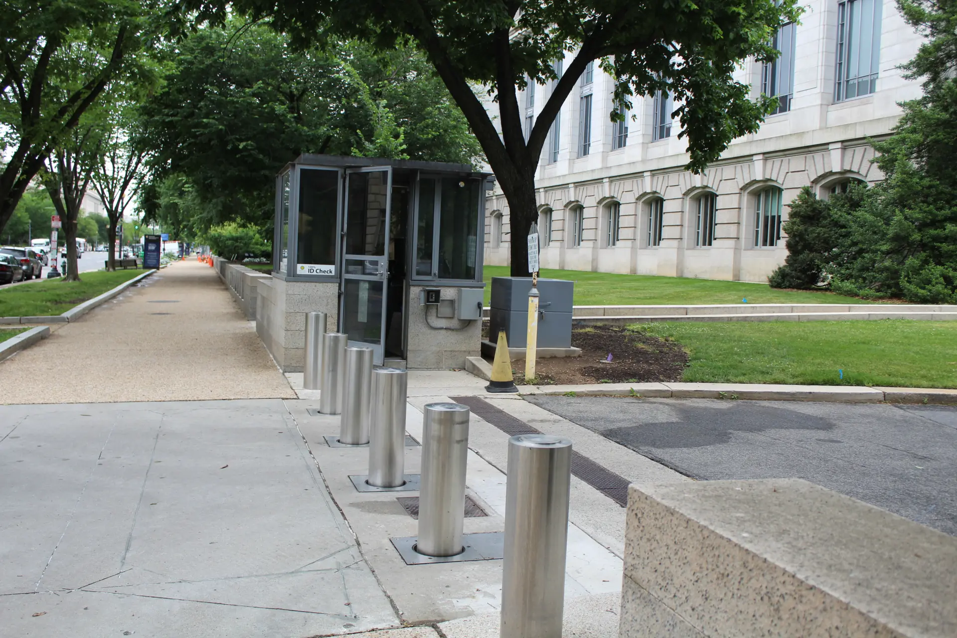 Silver bollards lining a driveway near a security booth and an institution building.