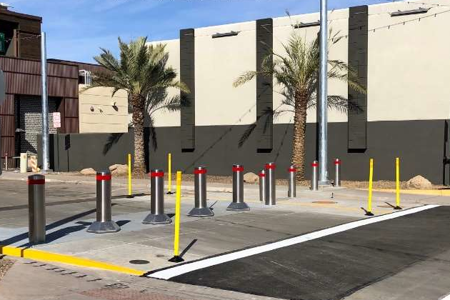 Stainless steel Matador bollards with red reflective bands installed on a sidewalk near palm trees.
