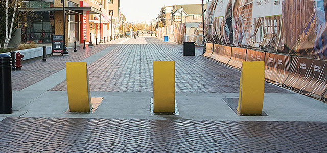 Three yellow bollards blocking vehicle access to a cobblestone pedestrian street.