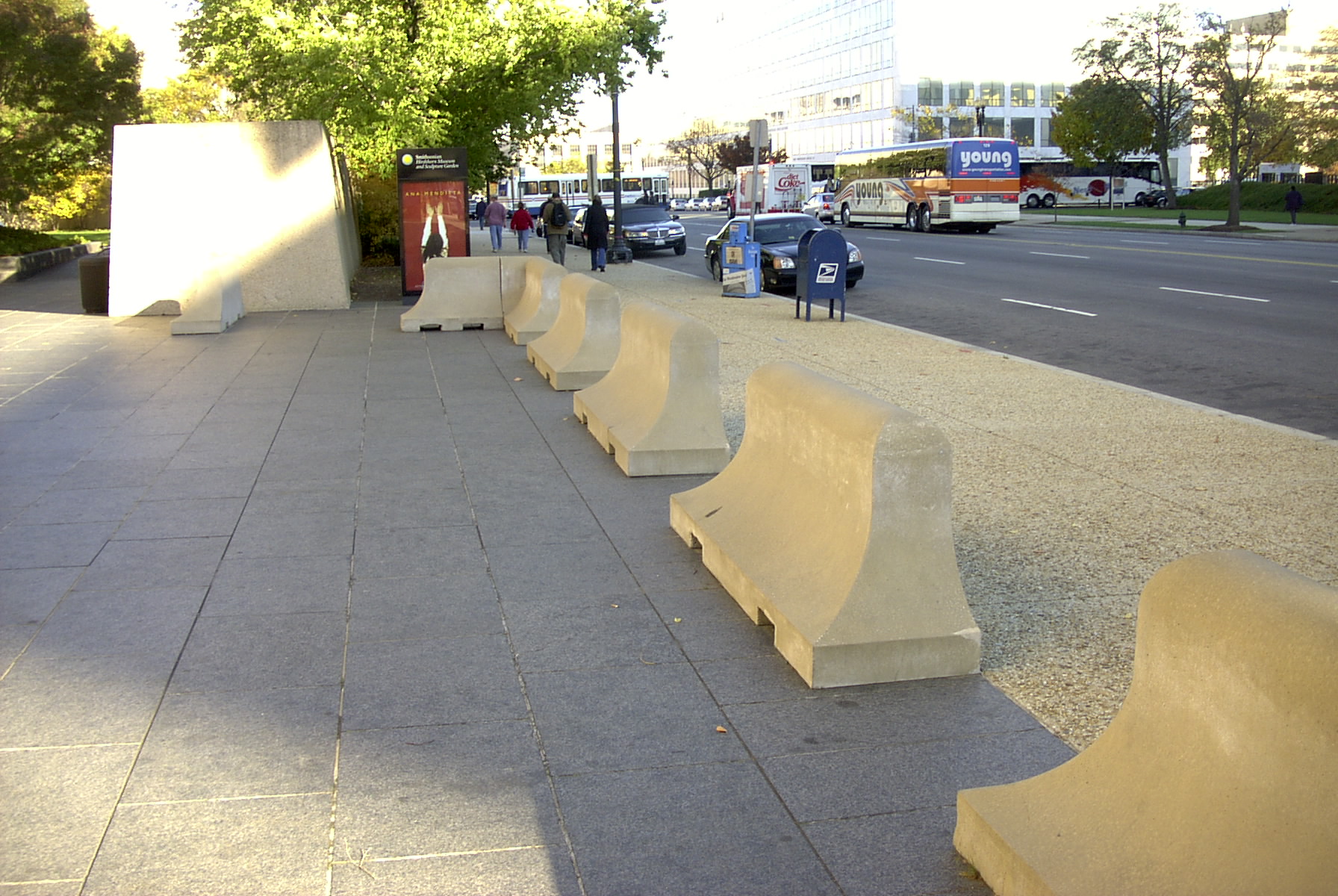 A row of curved concrete barriers lines the sidewalk near a city street.