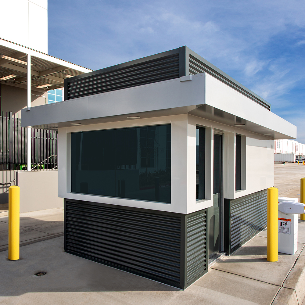 A sleek, modern security booth with tinted windows stands near a parking lot.