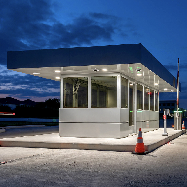 Illuminated guard booth with sleek design and cones nearby in a nighttime setting.