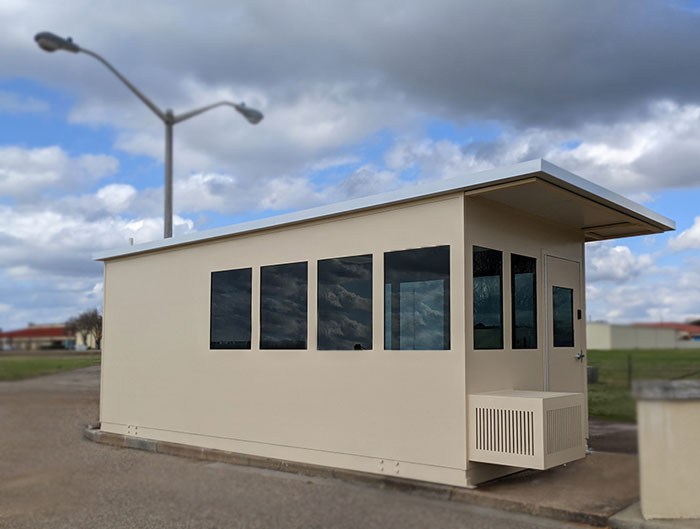 A beige rectangular security booth with large windows sits under a cloudy sky.