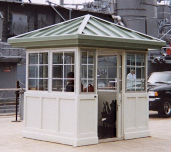 Traditional guard booth with a pitched green roof and a white frame near a vehicle.